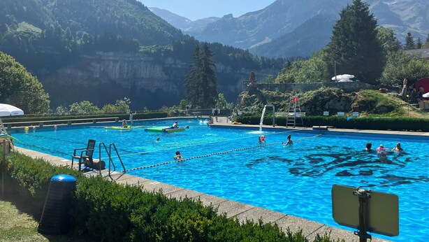 Una piscina con agua cristalina azul, rodeada de exuberante vegetación y montañas al fondo.