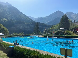 Una piscina con acqua cristallina blu, circondata da vegetazione lussureggiante e montagne sullo sfondo.