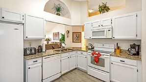 Una cocina con armarios blancos, microondas, estufa y lavabo.