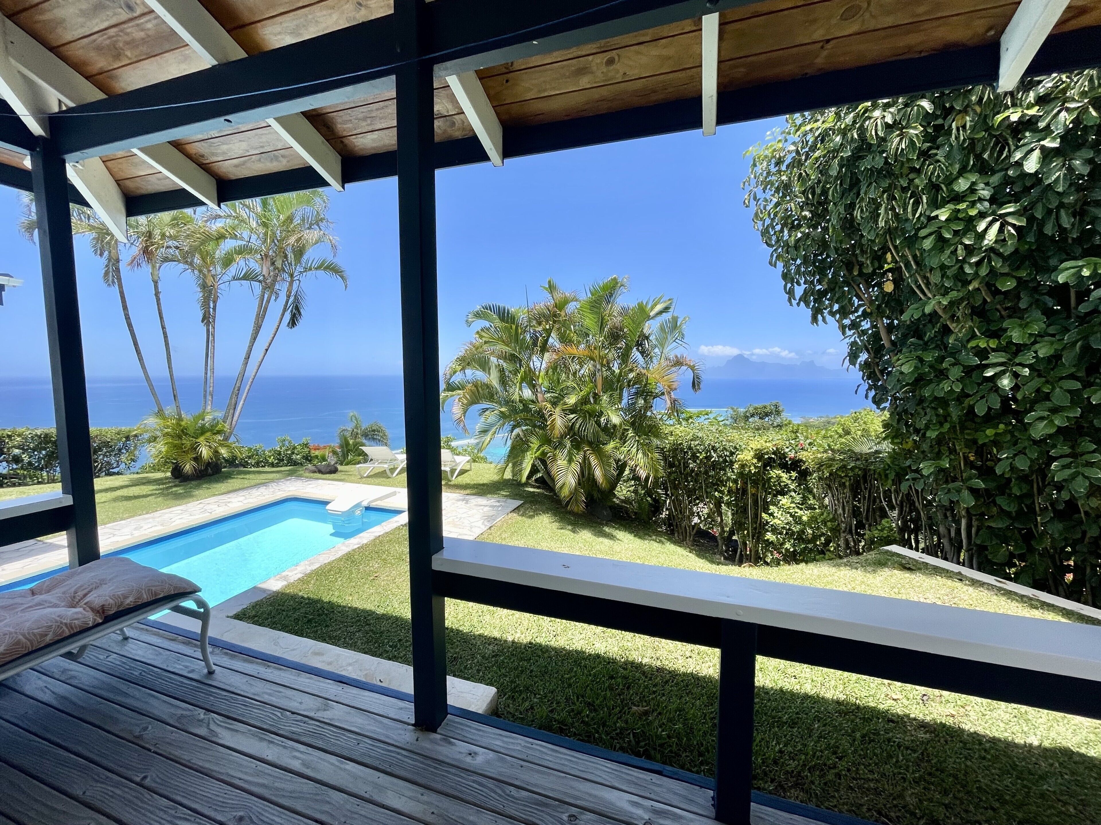 A wooden deck with a pool, lounge chairs, and a view of the ocean.