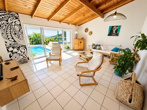 Amplia sala de estar con techo de madera, vista a la piscina y sofá estampado con motivos tropicales.