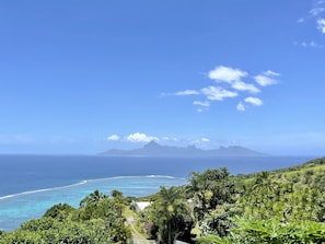 A tropical landscape with a clear view of the ocean, lush greenery, and a distant mountain range. - Villa Tiare | Punaauia • Private Pool • Panoramic Moorea View • 4 Bedrooms (PUNAAUIA)