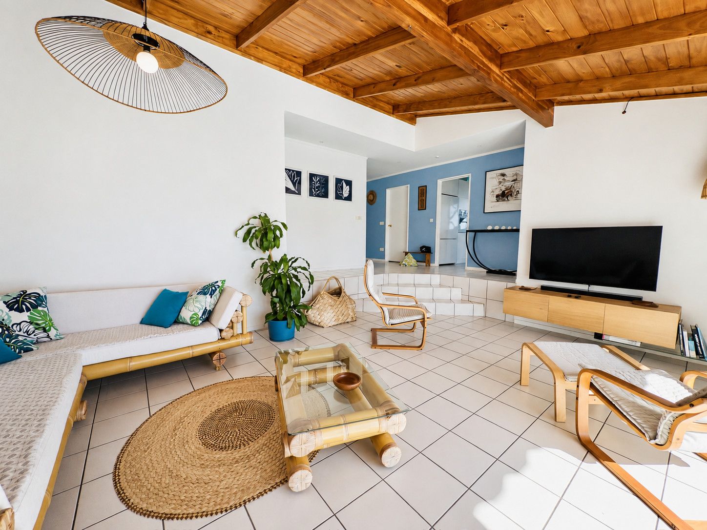 Ein modernes Wohnzimmer mit Holzboden, einer Couch mit Kissen, einem Couchtisch, einem Fernseher und einem Essbereich mit Fernseher.