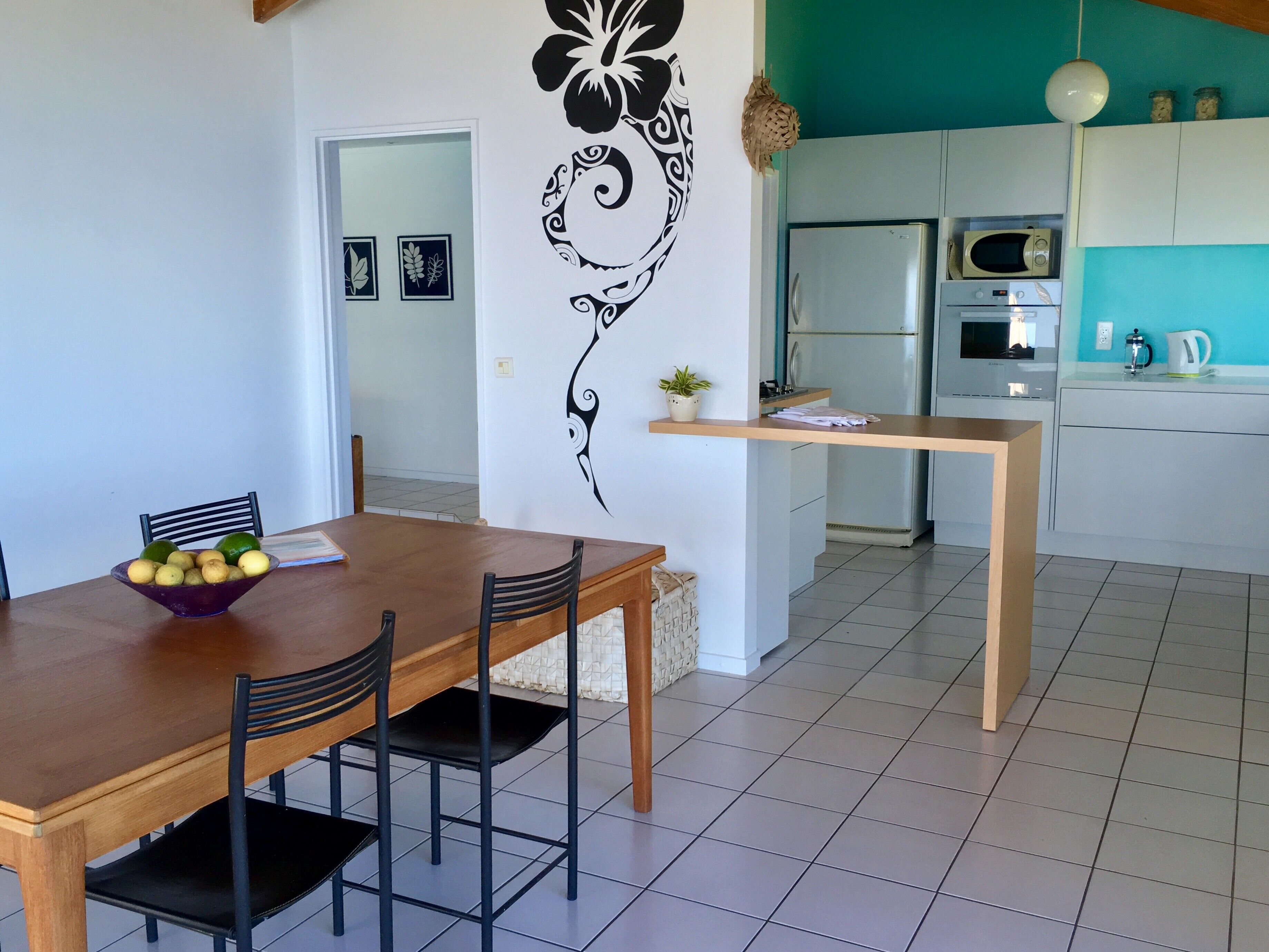 A dining area with a wooden table and chairs, a bowl of fruit, and a decorative wall piece.