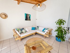 A room with a bamboo sofa, a woven coffee table, a potted plant, and a wall-mounted light fixture.