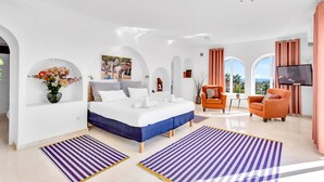 Een moderne hotelkamer met een groot bed, een televisie, een zithoek met een tafel en uitzicht op de omgeving.