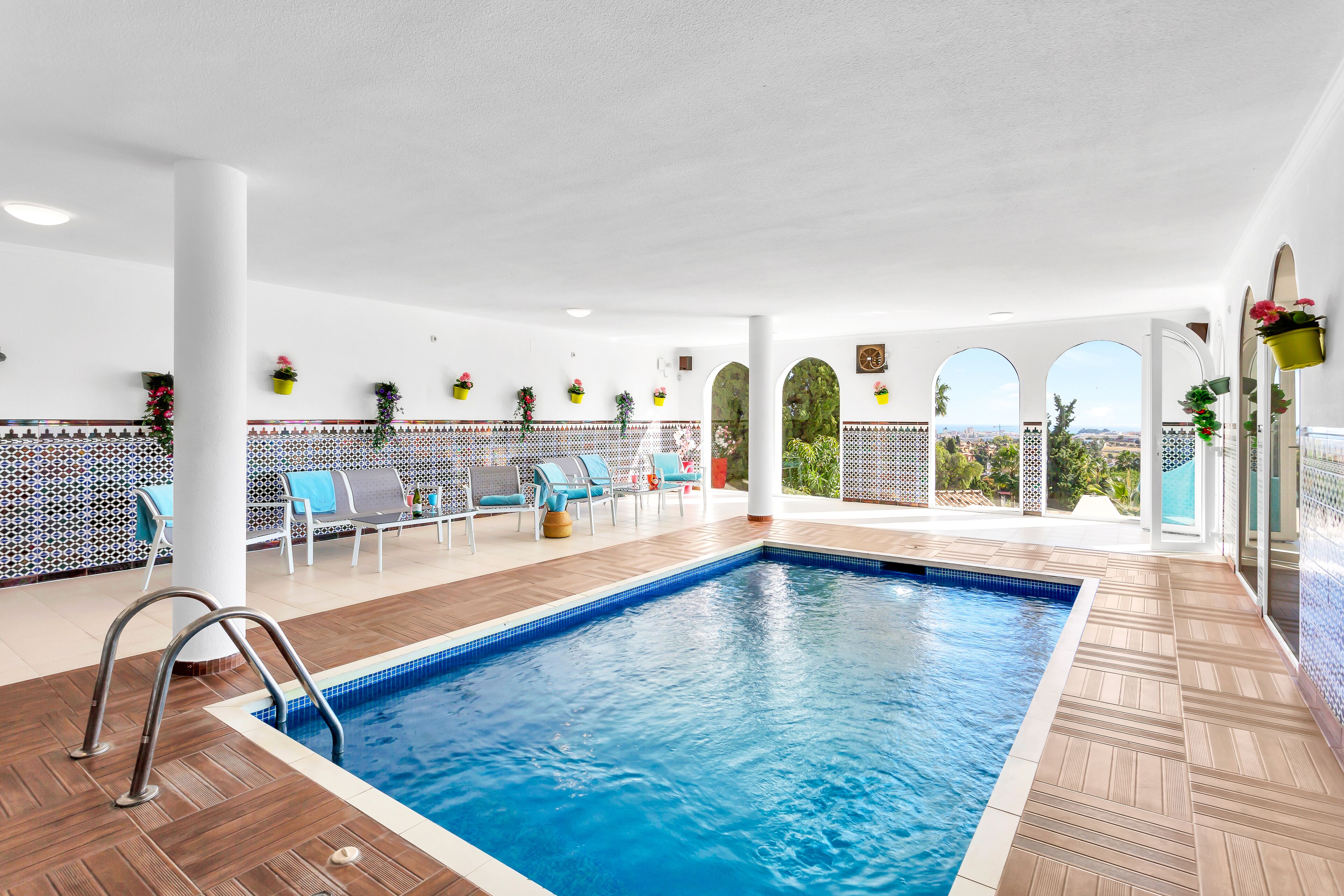 Una piscina interior con vistas a la ciudad, rodeada de sillones de descanso y plantas en macetas.