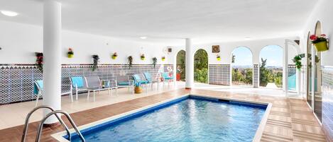Una piscina interior con vistas a la ciudad, rodeada de sillones de descanso y plantas en macetas.