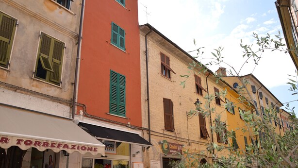 Una veduta di una strada con edifici dall'architettura tradizionale, caratterizzati da persiane e diversi tipi di facciate.