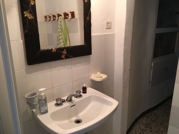 Un baño con un lavamanos blanco, un espejo con detalles de pan de oro y un perchero con una toalla verde.