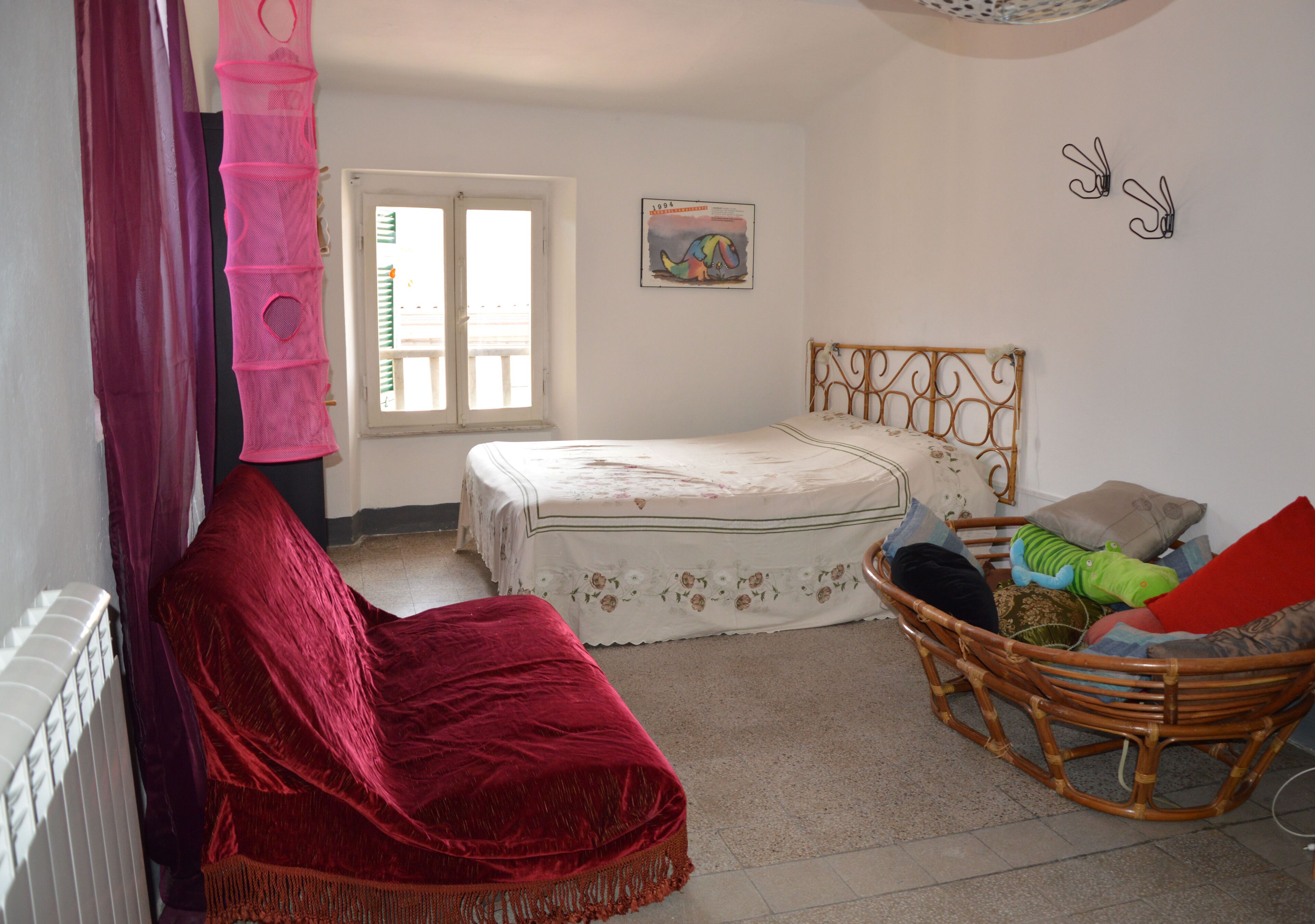 A bedroom with a bed, a rocking chair, a red chair, a window, and a wall decoration.
