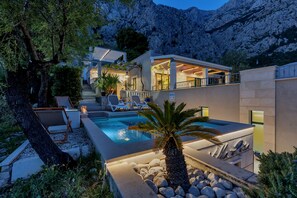 Ein modernes Haus mit Swimmingpool, Sitzgelegenheiten im Freien und Blick auf die Berge.