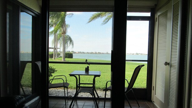 A room with a view of a grassy area and a body of water. There is a table and two chairs in the room.