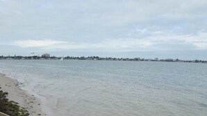 A beach with a staircase leading down to the water, a distant view of buildings, and a cloudy sky.