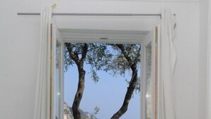 A room with a wooden table, a white chair, a vase with yellow flowers, and a view of a tree and the sea through a window. - Blessed villa directly on the sea. (Praiano)