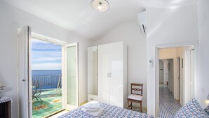 A bedroom with a bed, a chair, a wardrobe, and a view of the sea through an open door. - Blessed villa directly on the sea. (Praiano)