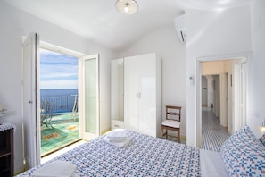 A bedroom with a bed, a chair, a wardrobe, and a view of the sea through an open door.