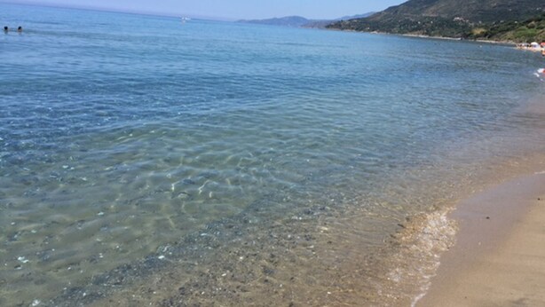 Una spiaggia con acque limpide e poco profonde, un litorale sabbioso e un paesaggio collinare sullo sfondo.