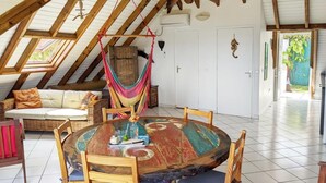 A cozy room with a wooden ceiling, a round wooden table, a hammock, and a white door.
