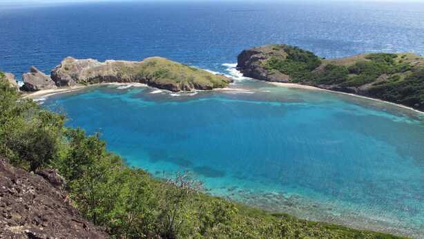 A coastal landscape with clear turquoise waters, rocky outcrops, and lush greenery.