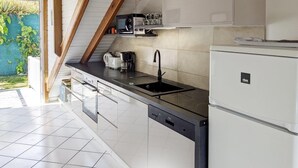 A modern kitchen with white cabinets, a black countertop, a built-in dishwasher, and a refrigerator.