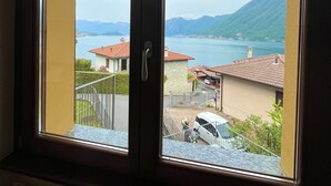 Ein Zimmer mit großem Fenster, das auf eine Wohngegend mit Häusern und einem Gewässer blickt.