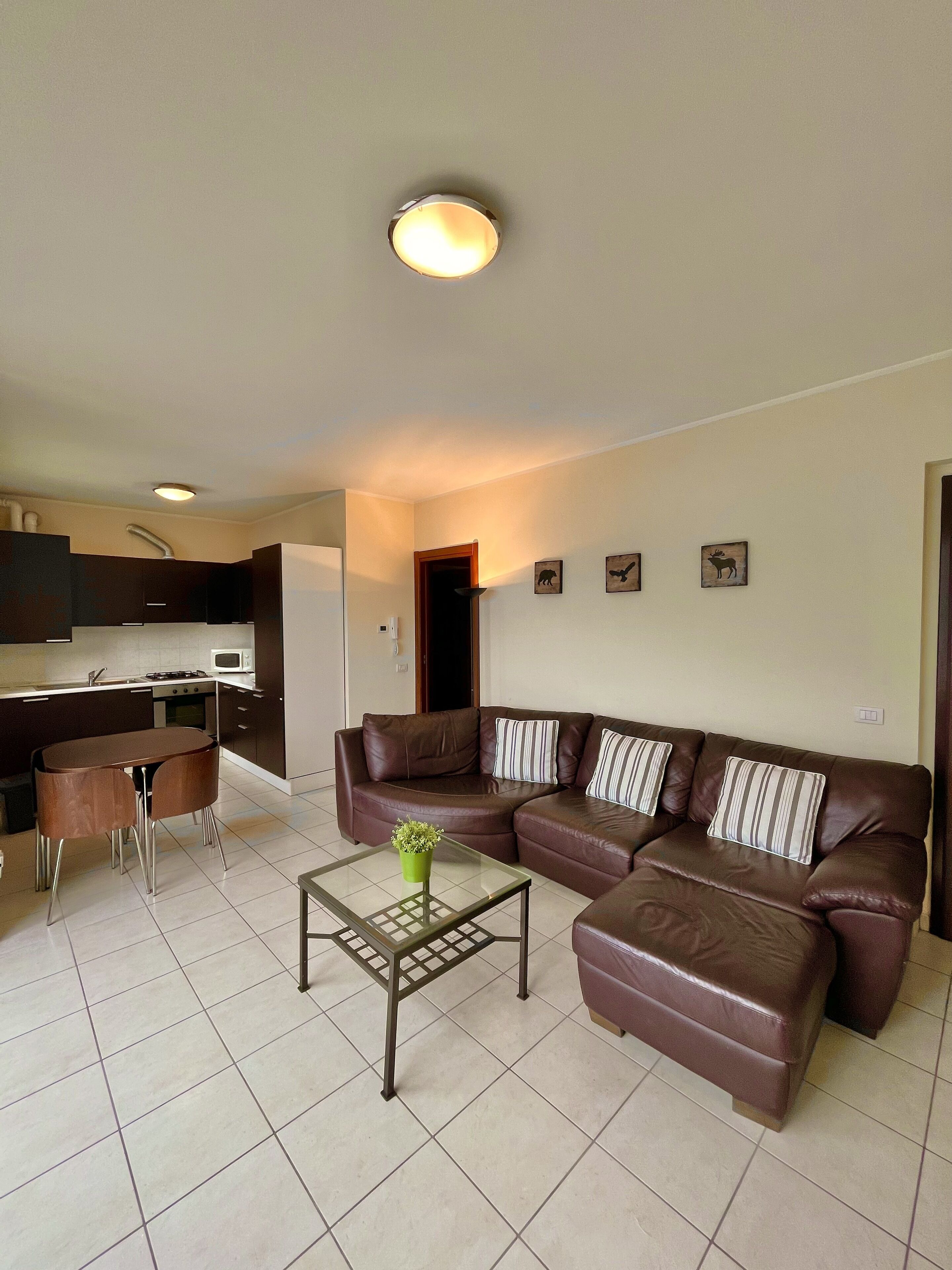 A living room with a brown leather sofa, a glass coffee table, and a kitchen area in the background.