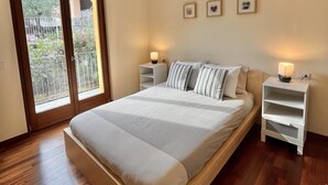 Ein Schlafzimmer mit einem großen Bett, zwei Nachttischen, einer Schiebetür zu einem Balkon und einem kleinen Regal.