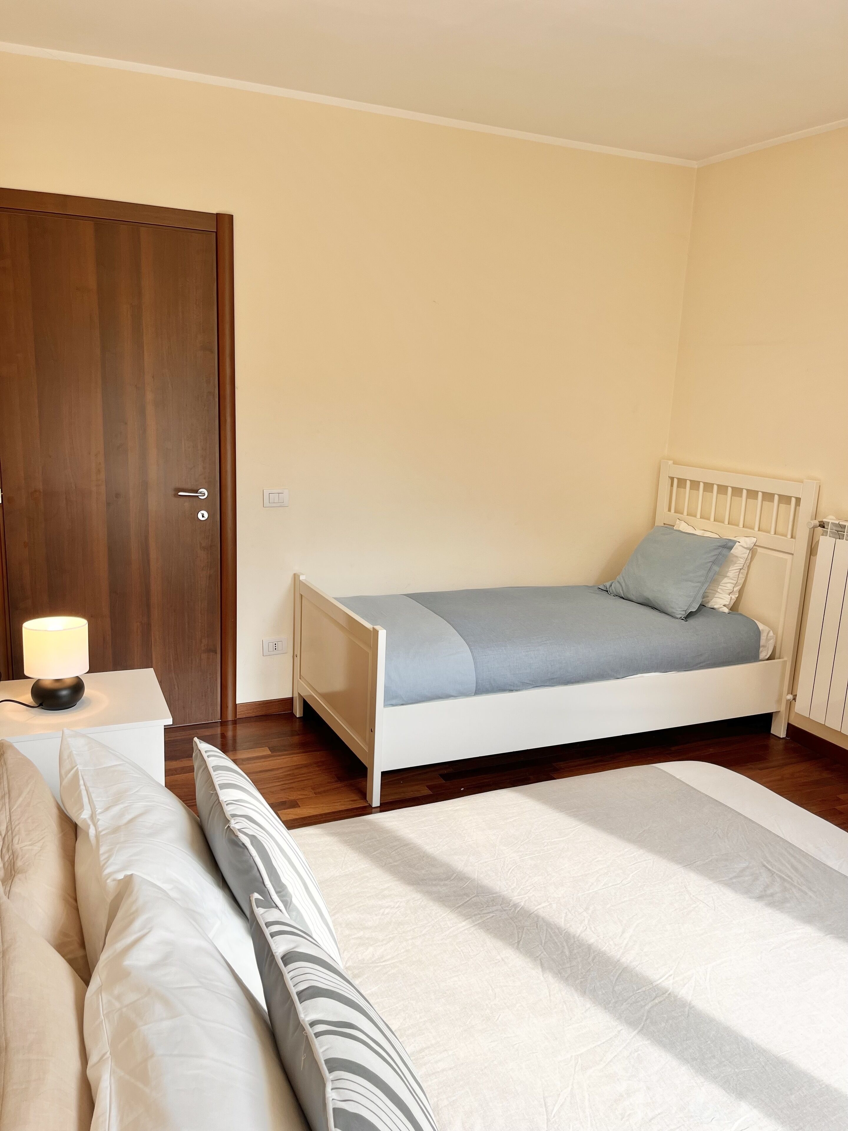 Ein Schlafzimmer mit einem Einzelbett, einem Nachttisch mit Lampe und einer Holztür.