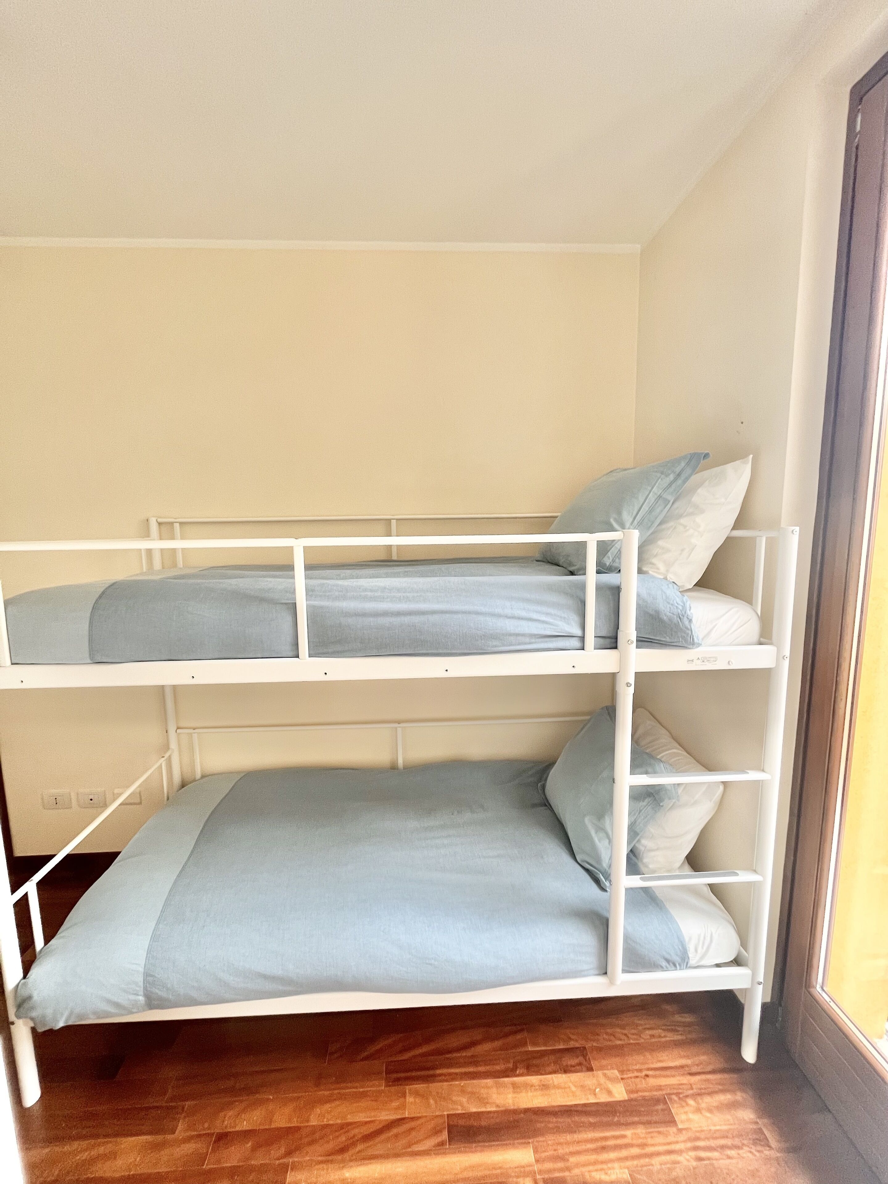 A bunk bed with two levels, white metal frame, and light blue bedding.