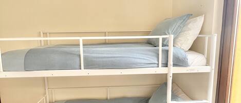 A bunk bed with two levels, white metal frame, and light blue bedding.
