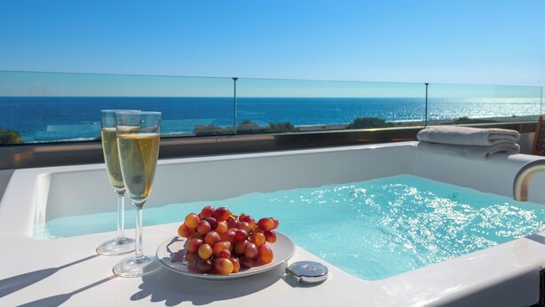 Hidromassatge amb vista despejada a l'oceà, un plat de raïm i dues copes de xampany.