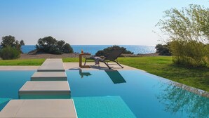 Una piscina amb escales cap a l'aigua, una cadira de relax i una taula amb vista al mar.