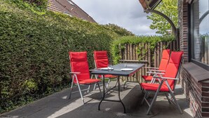 A patio with a table and four red chairs, surrounded by a hedge and a brick wall. - Pleasant and bright: The ground floor apartment with its ca. (Carolinensiel)