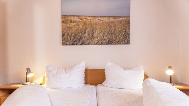 A double bed with white linens, two bedside lamps, a wooden headboard, and a framed landscape painting above. - Pleasant and bright: The ground floor apartment with its ca. (Carolinensiel)