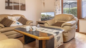 A living room with two leather sofas, a coffee table, a television, and a window with a view of trees. - Pleasant and bright: The ground floor apartment with its ca. (Carolinensiel)