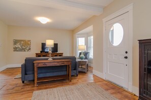 Ein Wohnzimmer mit einer Couch, einem Couchtisch, einem Fernseher und einer Lampe. Eine Tür mit rundem Fenster und ein Kamin sind ebenfalls vorhanden.