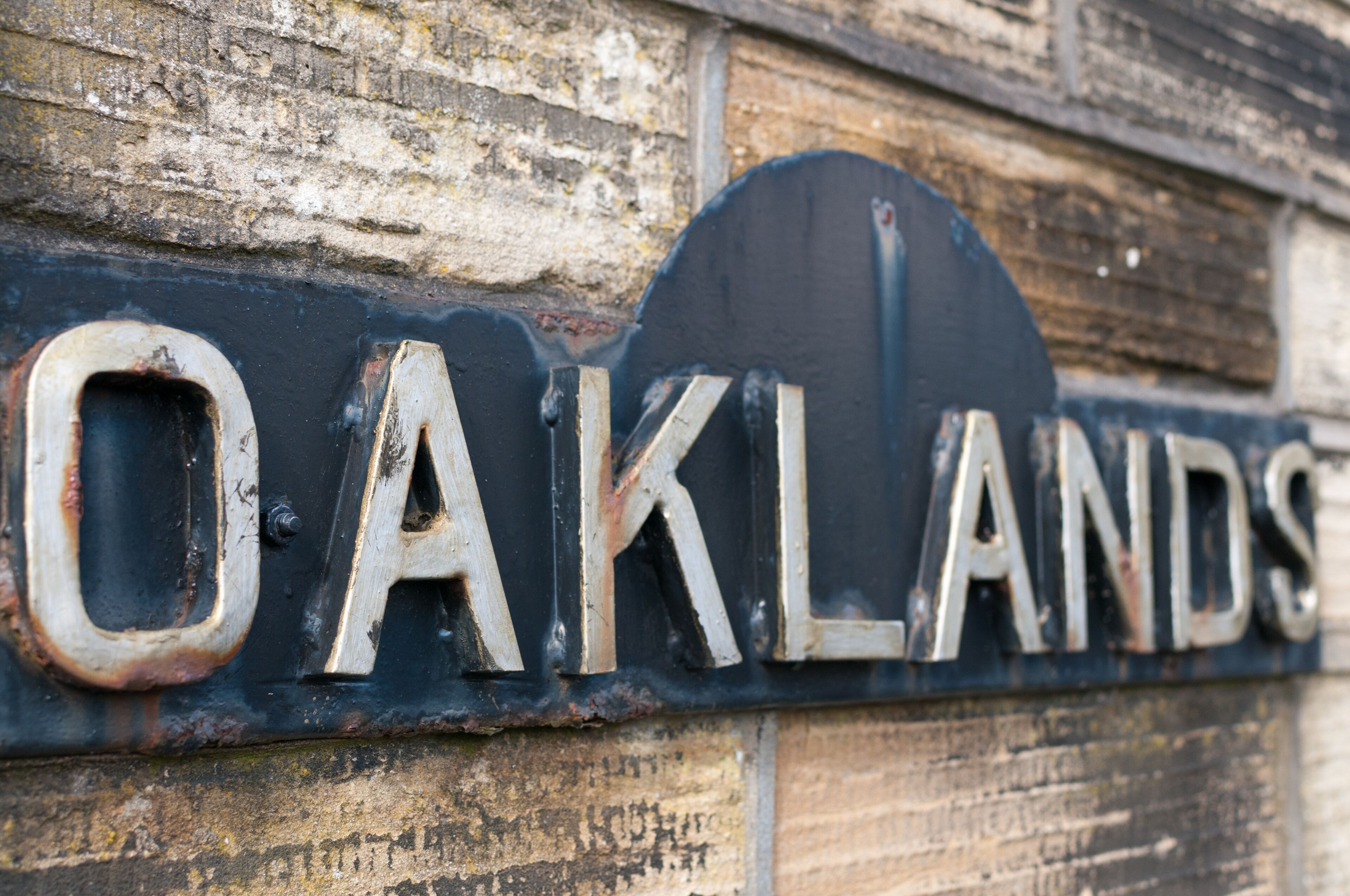 A weathered sign with the word "OAKLANDS" on a brick wall.