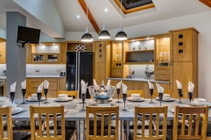 A modern kitchen with wooden cabinets, a black refrigerator, and a dining area set for six with wooden chairs and a central table. - Amazing Family House Sleeps 12 with  Private Hot Tub in Tranquil Location (Holmfirth)