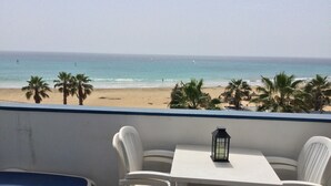 Un balcone con vista sulla spiaggia, sedie bianche, un tavolino e una lanterna.