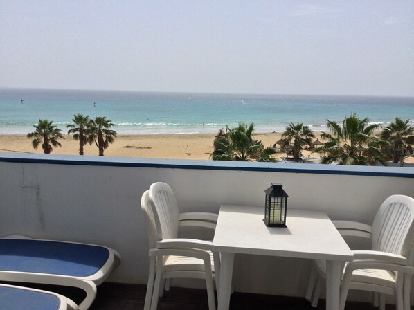 A balcony with a view of the beach, white chairs, a small table, and a lantern.