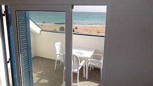 Un balcone con vista sulla spiaggia, sedie bianche e un tavolo.