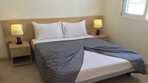 Un letto ben rifatto con una coperta blu a motivi, due cuscini bianchi e due abat-jour su comodini in legno.