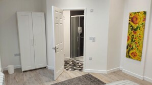 Una habitación con un armario blanco, una ducha con puerta de cristal, un suelo estampado y un cuadro en la pared.