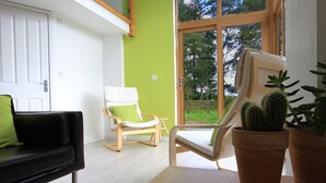 Una sala de estar moderna con un sofá negro, una silla de madera y un ventanal con vistas al verdor.