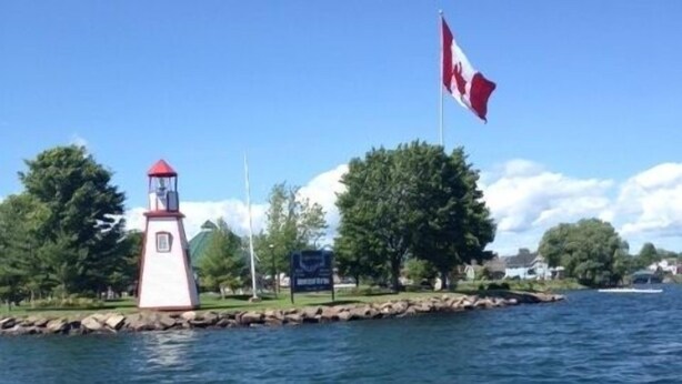 A lighthouse by a calm body of water with a Canadian flag flying. - Cottage For Rent-1000 Islands (Gananoque)