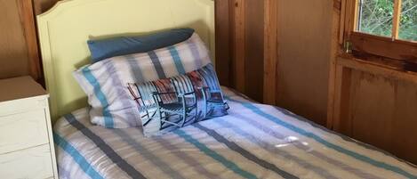 A wooden paneled room with a bed, a nightstand, and a window with blinds.