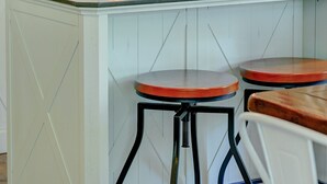Cozinha com armários brancos, geladeira de aço inoxidável e uma ilha pequena com banquetas.