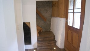 A narrow hallway with wooden flooring, a wooden door with glass panels, and a stone wall. - Rustico with style, modern and rustic, 2-4 P, in Val Poschiavo (Poschiavo)