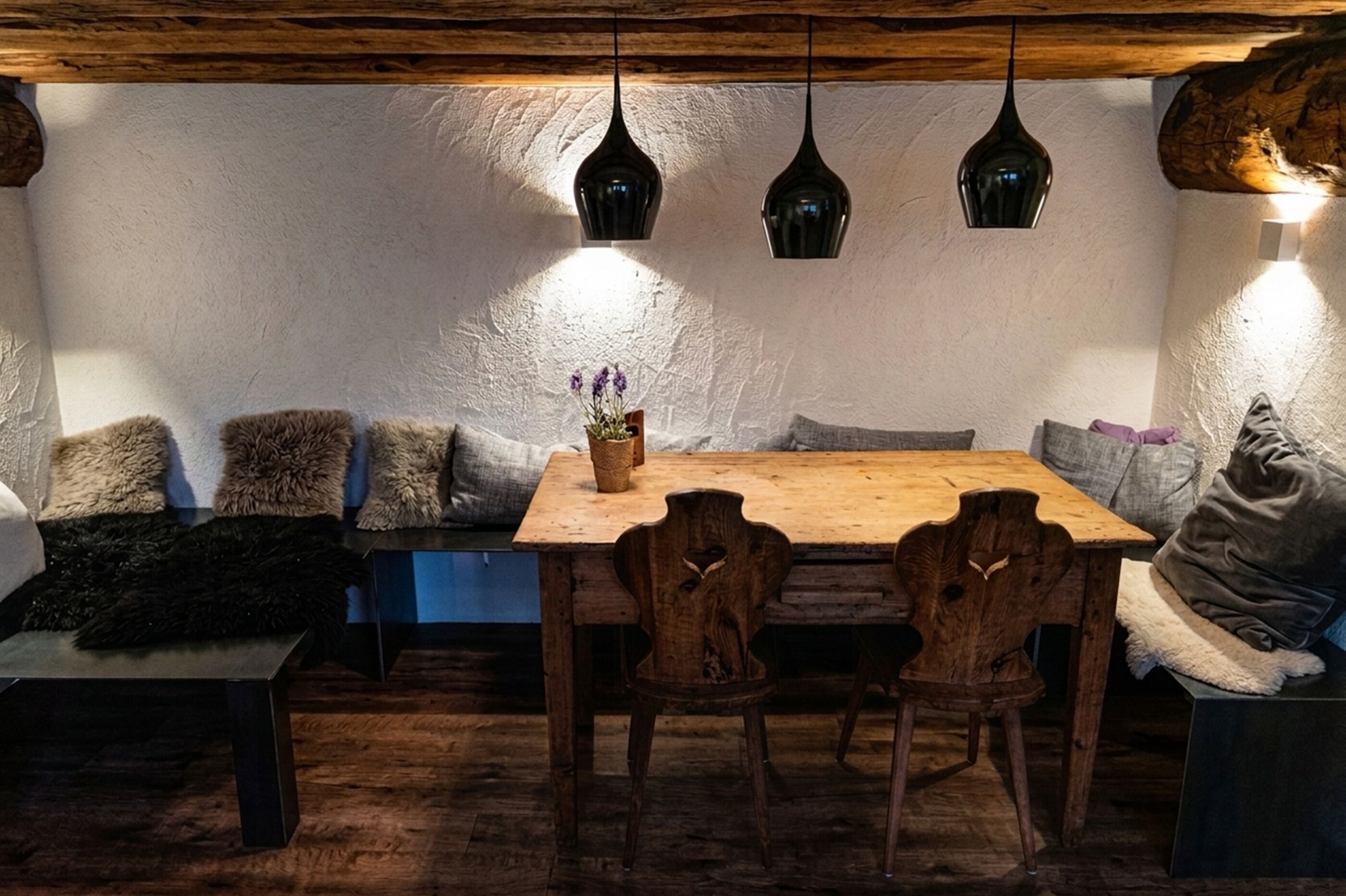 A cozy dining area with a wooden table and chairs, a bench with cushions, and pendant lights.